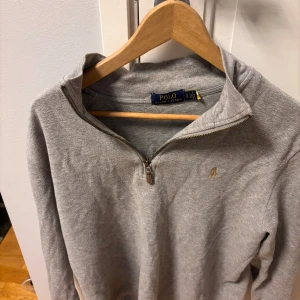 Grå tröja med dragkedja från Polo Ralph Lauren - Säljer denna pga att jag har växt ut den har haft den i ett år typ. Bra skicka förutom en vit fläck har inte försökt att ta bort den men skulle nog funka att få bort med starkare tvättmedel. Kom gärna med bud!!