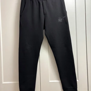 Svarta mjukisbyxor från EA7 - Snygga svarta mjukisbyxor från EA7 med elastisk midja och fickor fram och bak. Perfekta för en avslappnad stil. EA7-loggan är diskret placerad på framsidan.