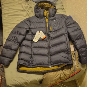 Svart dunjacka från LundHags - Säljer en svart dunjacka från Dunhags med dragkedja och hög krage. Jackan har en quiltad design och är perfekt för kalla dagar. Insidan är fodrad i en kontrasterande gul färg. Passar bra för vinterns äventyr.