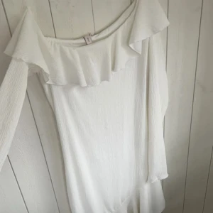 Vit klänning från Nelly - Säljer en stilren vit klänning från Nelly med offshoulder-design och volangdetaljer. Klänningen har långa ärmar. Materialet är lätt och bekvämt.