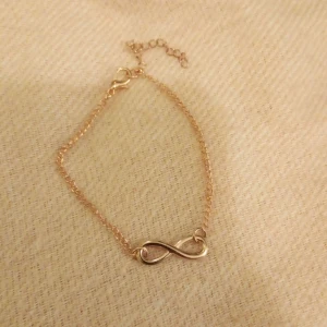 Guldarmband med oändlighetssymbol - Elegant guldarmband med en oändlighetssymbol i mitten. Armbandet har en fin kedja och justerbar längd med ett litet lås. Perfekt för att ge en subtil men stilfull touch till din outfit.