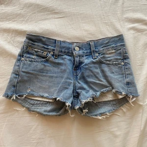 Blå jeansshorts från Levi's med låg midja - Snygga blå lågmidjade jeansshorts från Levi's med fransiga kanter och slitna detaljer. Midjemåttet=76cm Grenlängd=20cm