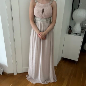 Ljusrosa balklänning med pärldetaljer - Elegant ljusrosa långklänning med pärldetaljer i midjan och en vacker nyckelhålsöppning framtill. Perfekt för bal eller annat event! Helt ny storlek 36, säljer samma klänning i svart!!!