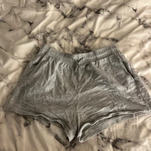 Grå bomullsshorts - Säljer ett par bekväma grå shorts i bomull med elastisk midja och dragsko. Perfekta för en avslappnad dag hemma eller lätt träning. Shortsen har en lös passform och sidofickor för extra funktionalitet.
