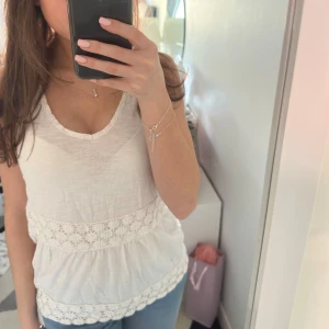 Vit  topp med spetsdetaljer - Säljer en söt vit ärmlös topp med v-ringning och fina spetsdetaljer. Toppen har en luftig passform och är tillverkad i ett mjukt material. Den är ganska gammal och kan därav inte se vad det är för storlek på lappen, men den passar mig bra och jag brukar ha S-XS☺️