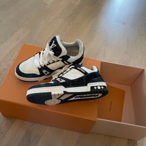 Svartvita sneakers från Louis Vuitton - Säljer ett par stilrena svartvita sneakers från Louis Vuitton. Skorna har en klassisk design med snörning och tydliga logodetaljer. Tillverkade i Italien, dessa sneakers kombinerar lyx och komfort perfekt. Helt nya använda endast 1 timme kvitto medföljer nypris 13800kr köpta i somras 