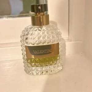 Valentino parfymflaska - Elegant parfymflaska från Valentino med ett lyxigt mönster av slipat glas. Flaskan har en gyllene etikett med märkesnamnet och en stilren svart spraytopp. Perfekt för den som vill ha en exklusiv doftupplevelse.