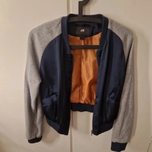 Blå och grå bomberjacka från H&M - Säljer en snygg bomberjacka från H&M i blått och grått. Jackan har långa ärmar och en dragkedja framtill. 
