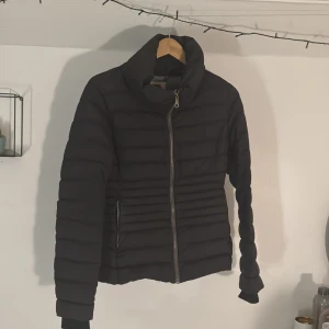 Svart dunjacka från Colmar - Säljer en snygg svart dunjacka från Colmar. Jackan har en dragkedja framtill och är långärmad med en stilren design. Perfekt för kyligare dagar med sin quiltade look. 🖤