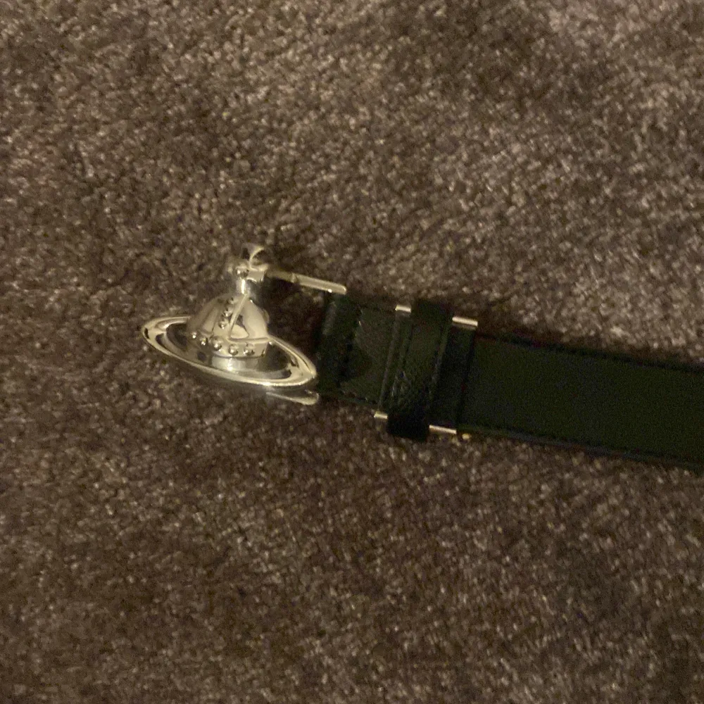 Snyggt svart bälte med en unik silverfärgad spänne i form av en planet. Perfekt för att ge en stilren touch till din outfit. Bältet är tillverkat i skinn och har en klassisk design.. Muu.