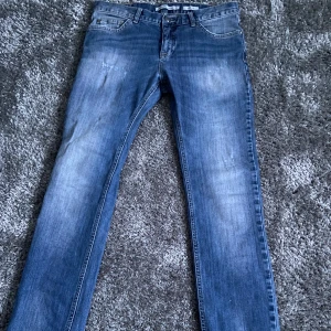 Blå jeansbyxor  - Snygga blå jeansbyxor med en klassisk straight passform. De har en midwaist design och är tillverkade i slitstarkt denim. Perfekta för en avslappnad stil med fem fickor och knappgylf.