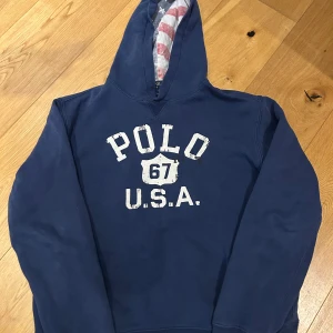 Blå hoodie från Ralph Lauren - Säljer en blå hoodie från Ralph Lauren med texten 'POLO 67 U.S.A.' tryckt på framsidan. 