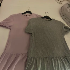 Lila och grå klänning - Två klänningar i lila och grått med korta ärmar och rund hals. De har en avslappnad passform med en lätt rynkad nederdel som ger en söt touch. Perfekta för en casual look. Båda är i storleken xs dam.