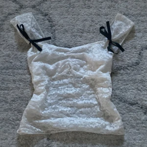 Vit spetslinne med svarta rosetter - Säljer en söt vit spetslinne med svarta rosetter på axelbanden. Använd gärna köp nu eller skriv vid frågor <3