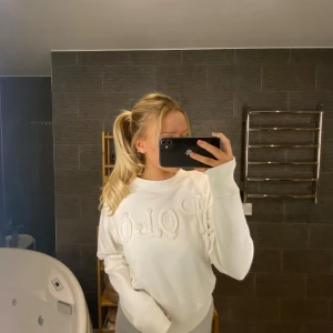 Vit sweatshirt Polo Ralph Lauren - Vit tröja från Polo Ralph Lauren med texten 'Polo' i ett rep-liknande mönster på framsidan.  