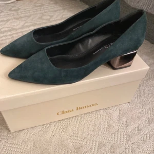 Gröna pumps från Violeta by Mango - Eleganta gröna pumps i mocka från Violeta by Mango med spetsig tå och unik metallisk klack. Perfekta för att ge en stilfull touch till din outfit.