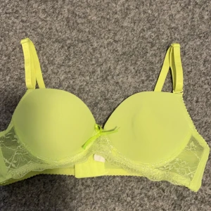 Neongul bh med spetsdetaljer - Snygg neongul bh med spetsdetaljer på sidorna och en liten rosett framtill. Justerbara axelband för perfekt passform. Perfekt för att liva upp garderoben med en färgklick!