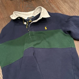 Blå och grön pikétröja från Ralph Lauren - Säljer en snygg blå och grön pikétröja från Ralph Lauren med vit krage och knappar. Tröjan har en broderad gul logotyp på bröstet. Perfekt för en stilren look. Storlek M i barnstorlek men passar ungefär Xs. Hör av mig vid funderingar nypris cirka 1500 mitt pris 399