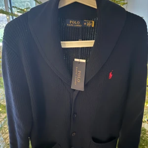 Mörkblå kofta från Ralph Lauren - Säljer en stilren mörkblå kofta från Ralph Lauren med klassisk krage och knappar framtill. 