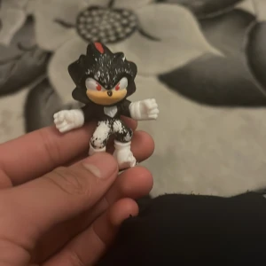 Svart och vit figurleksak med röda detaljer - En liten figurleksak i svart och vitt med röda detaljer. Figuren har en distinkt design med spetsiga former och vita handskar. Perfekt för samlare eller som en unik dekoration.