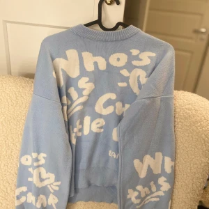 Ljusblå stickad tröja med text - Säljer en ljusblå stickad tröja med vit text och mönster. Tröjan har långa ärmar och en avslappnad passform. Perfekt för en mysig dag.