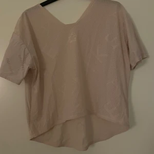Beige mesh-topp - Säljer en beige mesh-topp med korta ärmar och v-ringning. Toppen har en luftig design och är perfekt för varma dagar. Den är tillverkad i ett lätt och andningsbart material.