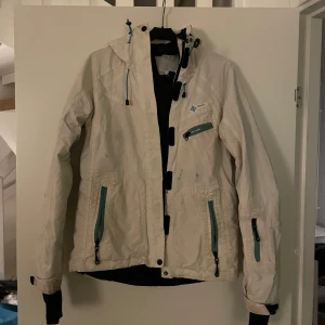 Vit vindjacka med dragkedjor - Säljer en vit vindjacka från H&M sports med turkosa dragkedjor och justerbar huva. Jackan har flera praktiska fickor och långa ärmar med svarta muddar. Perfekt för blåsiga dagar.
