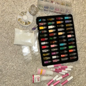 Nagelvårdsset med dekorationer och verktyg - Ett omfattande nagelvårdsset med olika dekorationer, glitter, nagellack, UV-lampor och verktyg för manikyr. Inkluderar flera färgglada glitterrör, nagelklippare, sax, pincett och nagelbandsverktyg. Perfekt för dig som vill ha allt till dina naglar hemma. Den som köper får med nagelkudde som din kund kan ha händerna på och massa klistermärken i jul, blommor och emojis motiv. Skriv för fler bilder 🩵