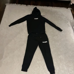 Svart mjukisset från Hoodrich - Säljer ett svart mjukisset från Hoodrich med både hoodie och byxor. Setet har en stilren design med Hoodrich-loggan tryckt på både tröjan och byxorna. Perfekt för en avslappnad stil. Mit pris 350kr nu pris 1200kr