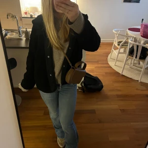 Svart teddyjacka från Stradivarius - Mysig svart teddyjacka från Stradivarius med huva och knappar. Perfekt för kyliga dagar med sin fluffiga och varma design. Jackan har en avslappnad passform och är lätt att matcha med olika outfits.