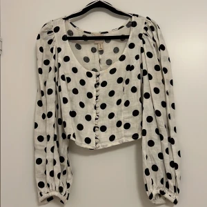Vit och svart prickig blus från H&M - Säljer en söt vit blus med svarta prickar från H&M. Blusen har långa ärmar och knappar framtill. Perfekt för en stilren och lekfull look.