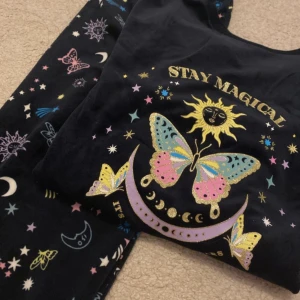 Multifärg pyjamas med magiskt tryck från Primark - Mysig pyjamas från Primark med ett färgglatt magiskt tryck av fjärilar, stjärnor och månar. Texten 'Stay Magical' pryder framsidan. Perfekt för en bekväm natt med en touch av magi.