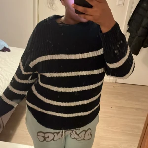 Mörkblå och vit randig stickad tröja - Mysig mörkblå och vit randig stickad tröja med långa ärmar. Perfekt för kyliga dagar och ger en avslappnad stil. Passar bra till jeans eller mjukisbyxor.