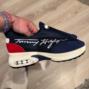 Blå sneakers  Tommy Hilfiger - Snygga blå sneakers från Tommy Hilfiger med vit och röd detalj på hälen. Skorna har en tjock sula och märkets logga i vitt på sidan. Storlek 38. (Köparen står för fraktenk) 