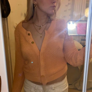 Orange korall stickad kofta - Säljer en söt  orangs stickad kofta med guldknappar. Koftan är croppad och har långa ärmar med ribbade muddar. Perfekt skick !