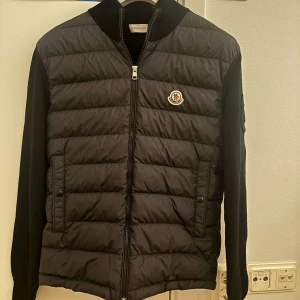 Svart quiltad jacka från Moncler - Snygg svart quiltad jacka från Moncler med dragkedja och broderad logga på bröstet. Jackan har långa ärmar och en stilren design som passar perfekt för kyligare dagar. Köpt på Room1006 i Malmö, KVITTO FINNS! Storlek 1