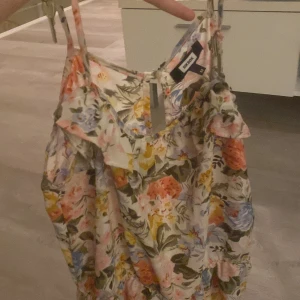 Blommig klänning från BikBok - Säljer en söt blommig klänning från BikBok med tunna axelband och volangdetaljer. Perfekt för sommarens varma dagar med sitt färgglada mönster i rosa, blått och grönt.