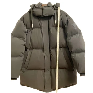 Svart pufferjacka från Ami - Säljer en svart pufferjacka från Ami med hög krage och justerbara dragsnören. Jackan har en stilren design med dolda fickor och en dragkedja framtill. Perfekt för kyliga dagar. Oversized! M-L