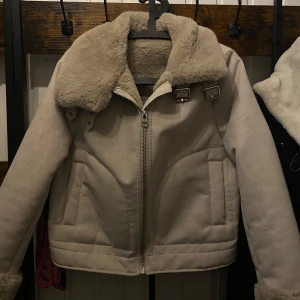 Beige jacka  - Säljer en snygg beige jacka med päls på kragen och insidan. Jackan har dragkedja framtill och spännen vid kragen för extra stil. Perfekt för kyliga dagar!