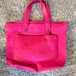 Rosa shoppingväska från Marc Jacobs - Snygg rosa shoppingväska från Marc Jacobs med praktisk dragkedja framtill. Perfekt för en dag på stan eller som en färgglad accessoar. Väskan har två handtag och gott om plats för dina saker.