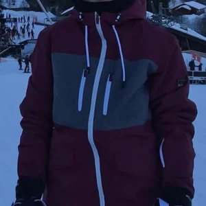 Röd och grå vinterjacka från Dr. Zipe - Säljer en snygg och varm vinterjacka från Dr. Zipe i röd och grå färg. Jackan har en praktisk dragkedja och flera fickor med dragkedjor för säker förvaring. Den är perfekt för kalla vinterdagar och har en skön passform med justerbar huva. Insidan är fodrad för extra värme.