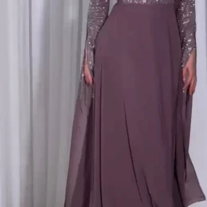 Lila långklänning med pärldetaljer - Elegant lila långklänning med glittrande pärldetaljer på ärmar och hals. Klänningen har långa ärmar och ett matchande bälte i midjan. Perfekt för speciella tillfällen.