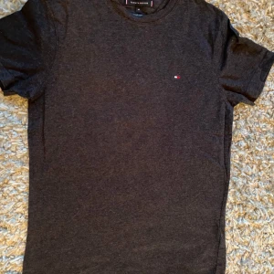 Mörkgrå t-shirt från Tommy Hilfiger - Snygg mörkgrå t-shirt från Tommy Hilfiger med liten logga på bröstet. Perfekt för en stilren och avslappnad look.