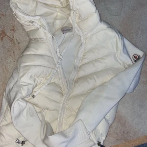 Vit dunjacka från Moncler - Snygg vit dunjacka från Moncler med huva och dragkedja. Jackan har en quiltad design och ribbade muddar vid ärmsluten. Perfekt för kyliga dagar.