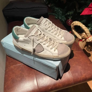 Beige sneakers från Philippe Model - Snygga beige sneakers från Philippe Model med grön detalj på hälen.  Dem är i 9/10 skick. Allt OG följer med. Säljer dem för att dem inte passar längre. Skorna är i storlek 40 men dem sitter rätt stora så skulle passa upp till 41,5. Priset är inte skrivet i sten. Har ni några frågor är det bara att skriva, kan vara öppen för byten