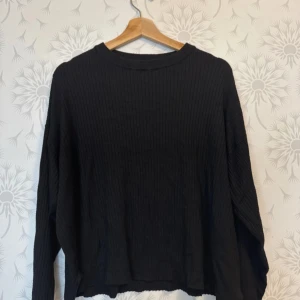 Svart ribbad tröja - Säljer en stilren svart ribbad tröja med lång ärm. Perfekt för en avslappnad look. Tröjan har en lös passform och är gjord i ett mjukt material.