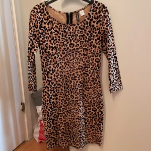 Leopardmönstrad klänning från H&M Divided - Snygg leopardmönstrad klänning från H&M Divided med trekvartsärm och dragkedja i ryggen. Perfekt för en djärv look!
