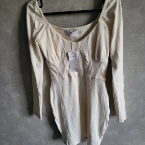 Vit klänning från House Brand - Snygg vit klänning från House Brand med långärmad design och ribbad struktur. Klänningen har en elegant passform och är tillverkad med miljövänliga material. Perfekt för en stilren look.