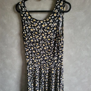 Blommig klänning från Clek - Söt blommig klänning från Clek i svart med vita och gula blommor. Klänningen är ärmlös och har en rund halsringning. Perfekt för en somrig look! Mjuk och väldigt bekväm! 