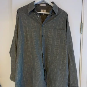 Grå rutig skjorta - Snygg grå rutig skjorta med klassisk krage och knappar framtill. Skjortan har långa ärmar och en bröstficka. Perfekt för en stilren look.